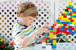 Little blond child and kid boy playing with lots of colorful plastic blocks.