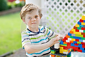 Little blond child and kid boy playing with lots of colorful plastic blocks.