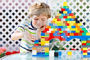 Little blond child and kid boy playing with lots of colorful plastic blocks.