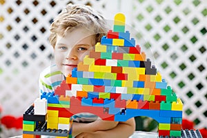 Little blond child and kid boy playing with lots of colorful plastic blocks.