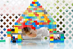 Little blond child and kid boy playing with lots of colorful plastic blocks.