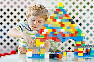 Little blond child and kid boy playing with lots of colorful plastic blocks.