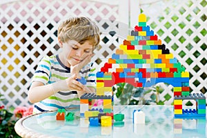 Little blond child and kid boy playing with lots of colorful plastic blocks.