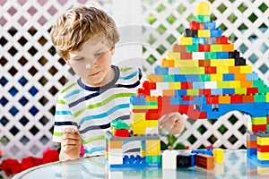 Little blond child and kid boy playing with lots of colorful plastic blocks.