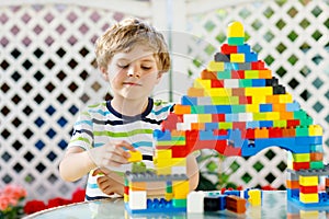 Little blond child and kid boy playing with lots of colorful plastic blocks.