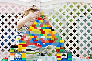 Little blond child and kid boy playing with lots of colorful plastic blocks.