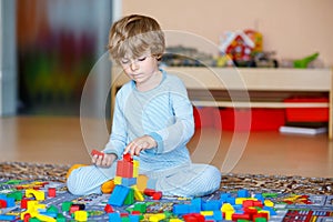 Little blond child playing with colorful wooden blocks indoor