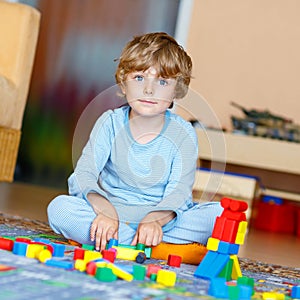 Little blond child playing with colorful wooden blocks indoor