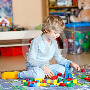 Little blond child playing with colorful wooden blocks indoor