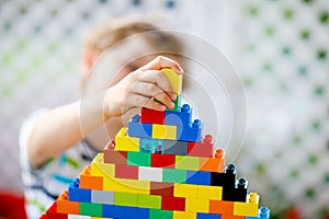 Little blond child playing with lots of colorful plastic blocks. Adorable preschool kid boy wearing colorful shirt and