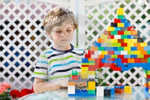 Little blond child playing with lots of colorful plastic blocks. Adorable preschool kid boy wearing colorful shirt and