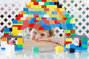 Little blond child playing with lots of colorful plastic blocks. Adorable preschool kid boy wearing colorful shirt and