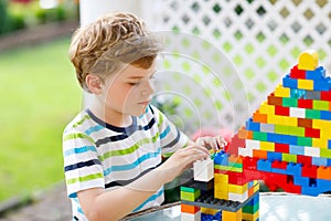 Little blond child playing with lots of colorful plastic blocks. Adorable preschool kid boy wearing colorful shirt and