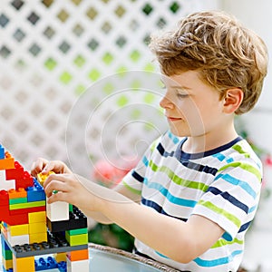 Little blond child playing with lots of colorful plastic blocks. Adorable preschool kid boy wearing colorful shirt and