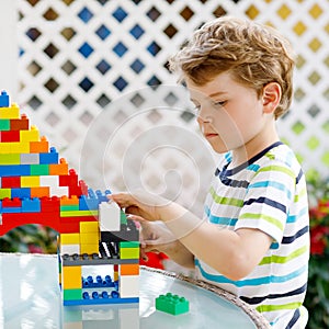 Little blond child playing with lots of colorful plastic blocks. Adorable preschool kid boy wearing colorful shirt and