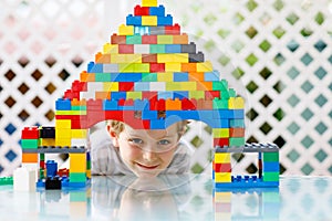 Little blond child playing with lots of colorful plastic blocks. Adorable school kid boy wearing colorful shirt and