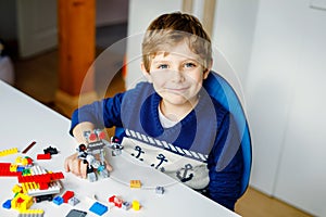 Little blond child playing with lots of colorful plastic blocks. Cute school kid boy having fun with building and