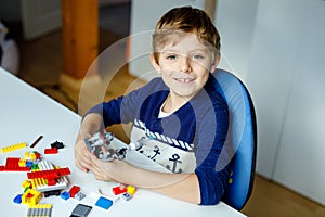 Little blond child playing with lots of colorful plastic blocks. Cute school kid boy having fun with building and