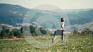Little Blond Child Running with a Badminton Racket Across a Mountain Meadow