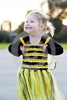 Little blond girl in bee costume dancing outdoors