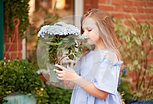 Little blond girl in blue dress with flowers nearby flowers store