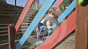 Little blond girl climbing the stairs to children`s slide at playground