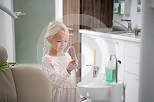 A little blond girl in the dental clinic. A cup with sterile water for rinsing the mouth in the foreground. A visit to a