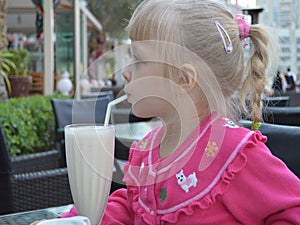 A little blond girl drinks a testy milkshake.