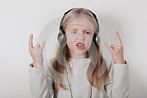 Blond girl with headphones listening music and singing. Cute little girl making a rock-n-roll sign.