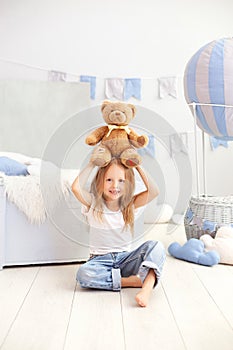 Little blond girl holding a teddy bear on the background of a decorative balloon. The child plays in the children`s room with toys