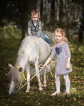 Little blond girl leading pony by bridle with her younger brother