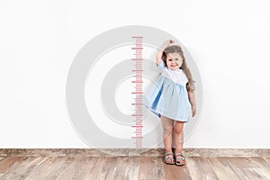 Little blond girl measuring height on white wall.