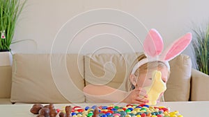 Little blond girl with rabbit ears plays with a chocolate bunny