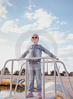 Little blond girl with raised arms blue cloudy sky background. Happy child smiling flying in the air. Lifestyle photo
