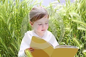 Little blond girl reading book green spikes garden