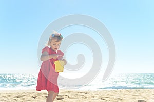 Little blond girl in red dress on the beach