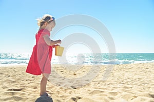 Little blond girl in red dress on the beach