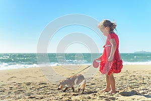 Little blond girl in red dress with dog on the beach