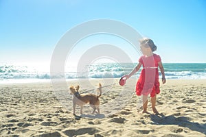 Little blond girl in red dress with dog on the beach