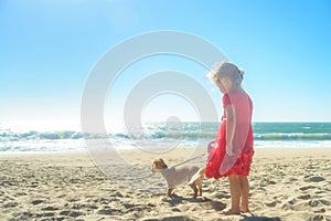 Little blond girl in red dress with dog on the beach