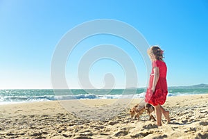 Little blond girl in red dress with dog on the beach