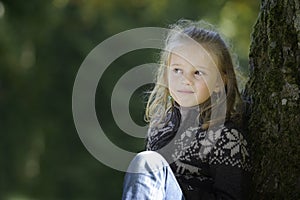 Little blond girl seated against a tree