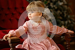 Little blond girl sits in a chair in front of Christmas tree