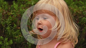 Little blond girl is smiling and closing her mouth with her hand in amazement