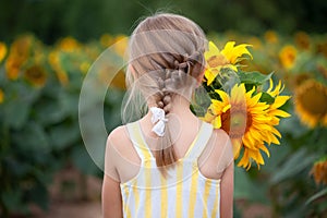 Little blond girl in a straw hat with a bouquet of sunflowers in the background of a field of sunflowers