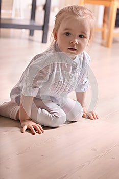 Little blond girl in striped shirt sitting on wooden floor