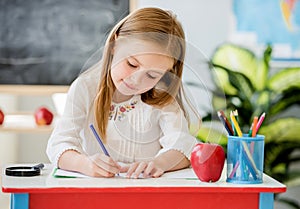 Little blond girl writing classwork in the school classroom