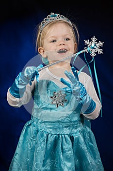 A little blond happy girl, dressed as Disney Frozen Princess Elsa.