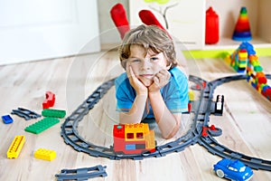 Little blond kid boy playing with colorful plastic blocks and creating train station