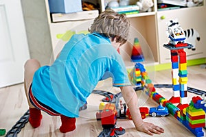 Little blond kid boy playing with colorful plastic blocks and creating train station